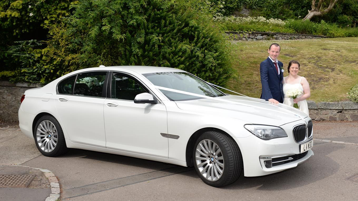 White BMW decorated with wedding ribbons with Bride and Groom standing by the vehicle