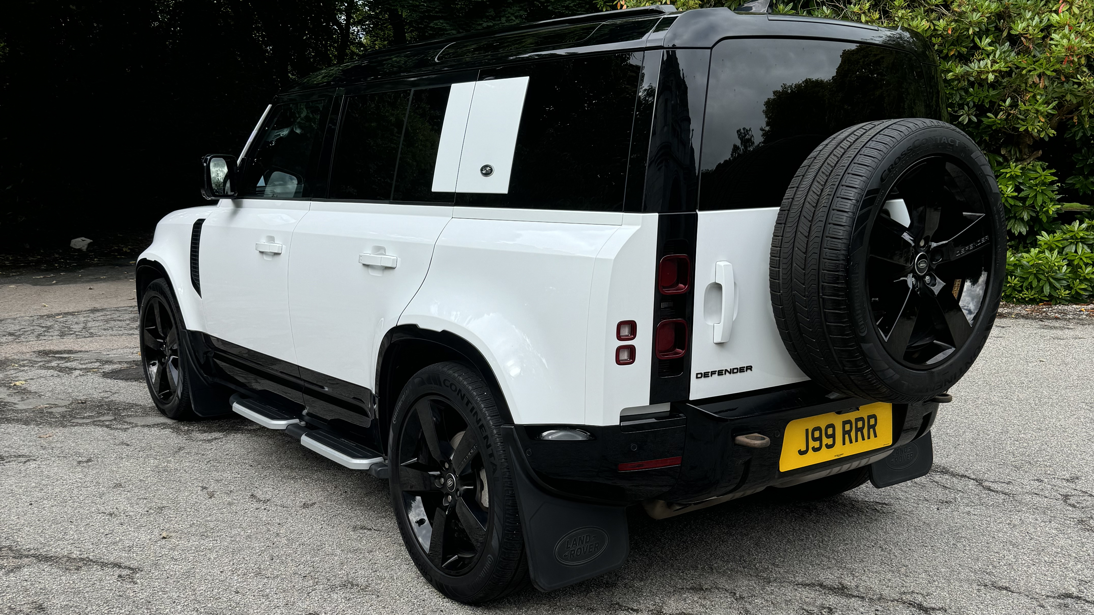 Rear Left side view of White Land rover Defender with Black Roof and Large Black Alloy wheels attached to rear boot