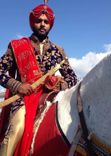 Asian Groom wearing traditional ceremonial outfit holding a gold sword sitting on top of a white horse