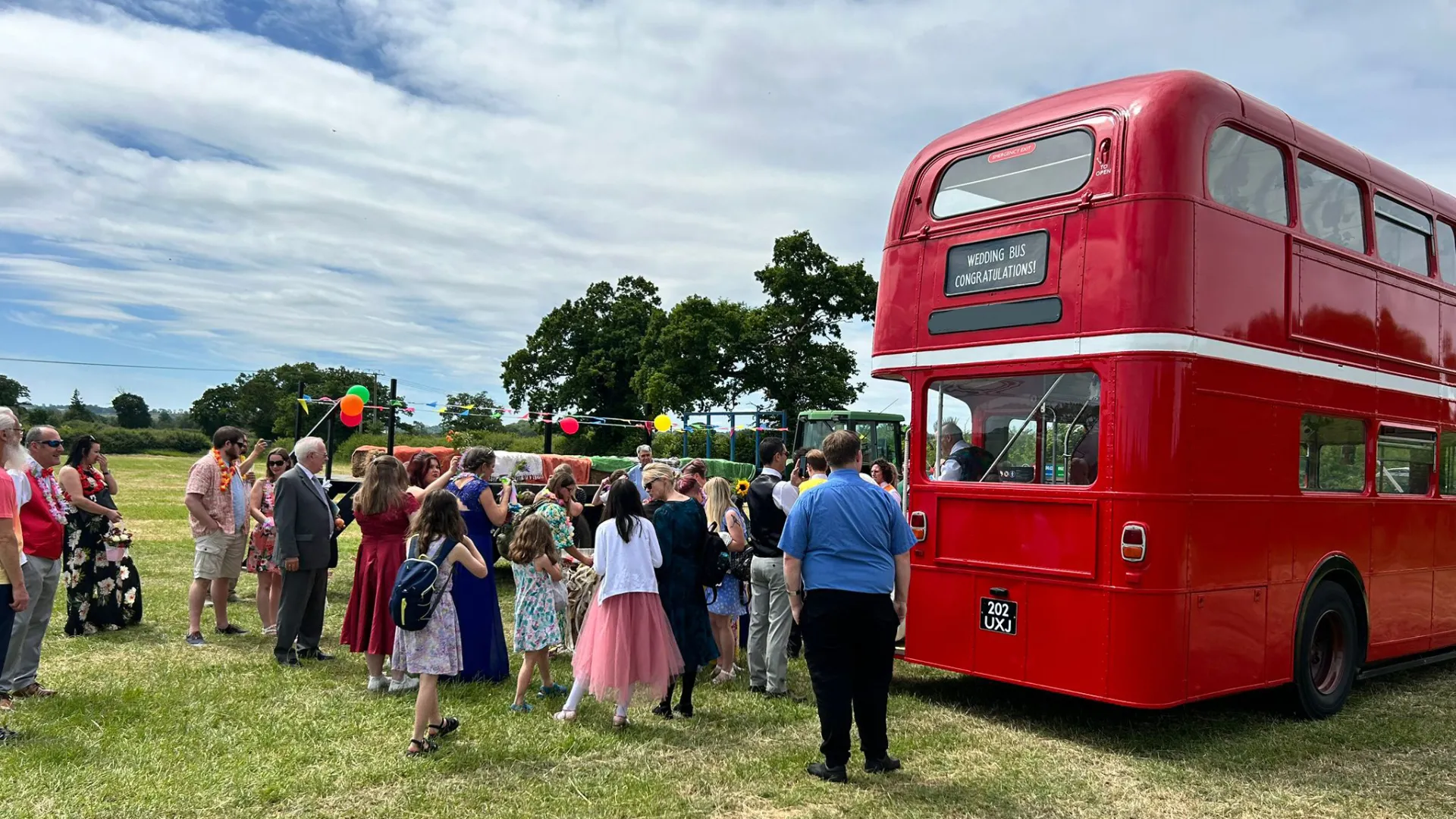 Red Double Decker Vintage Bus parked in a field with wedding guests around the bus