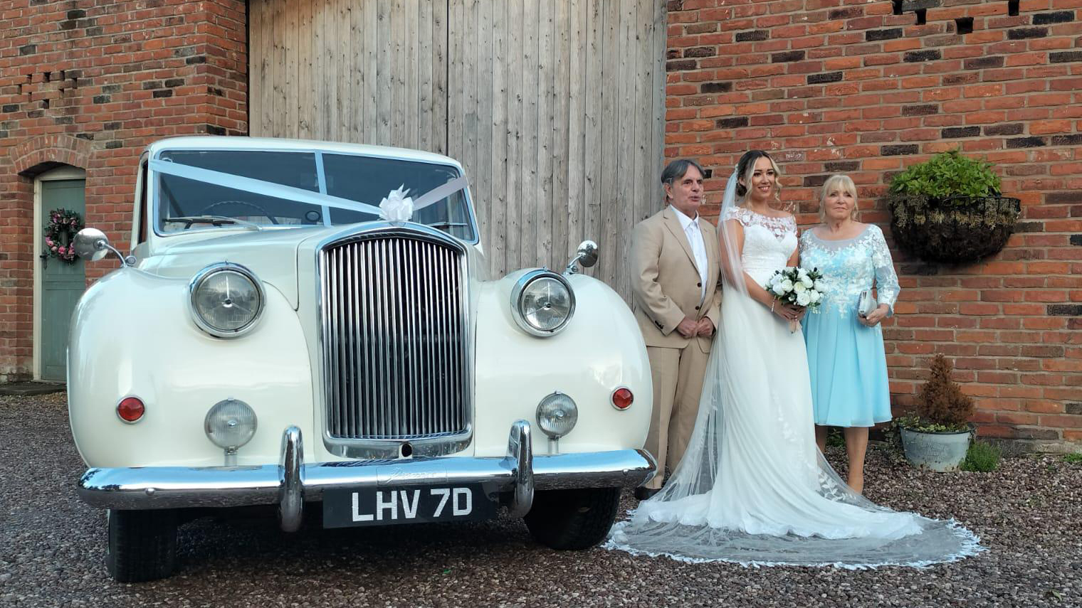 Bride and her parents standing by a White Classic Austin Princess Limousine decorated with white ribbons