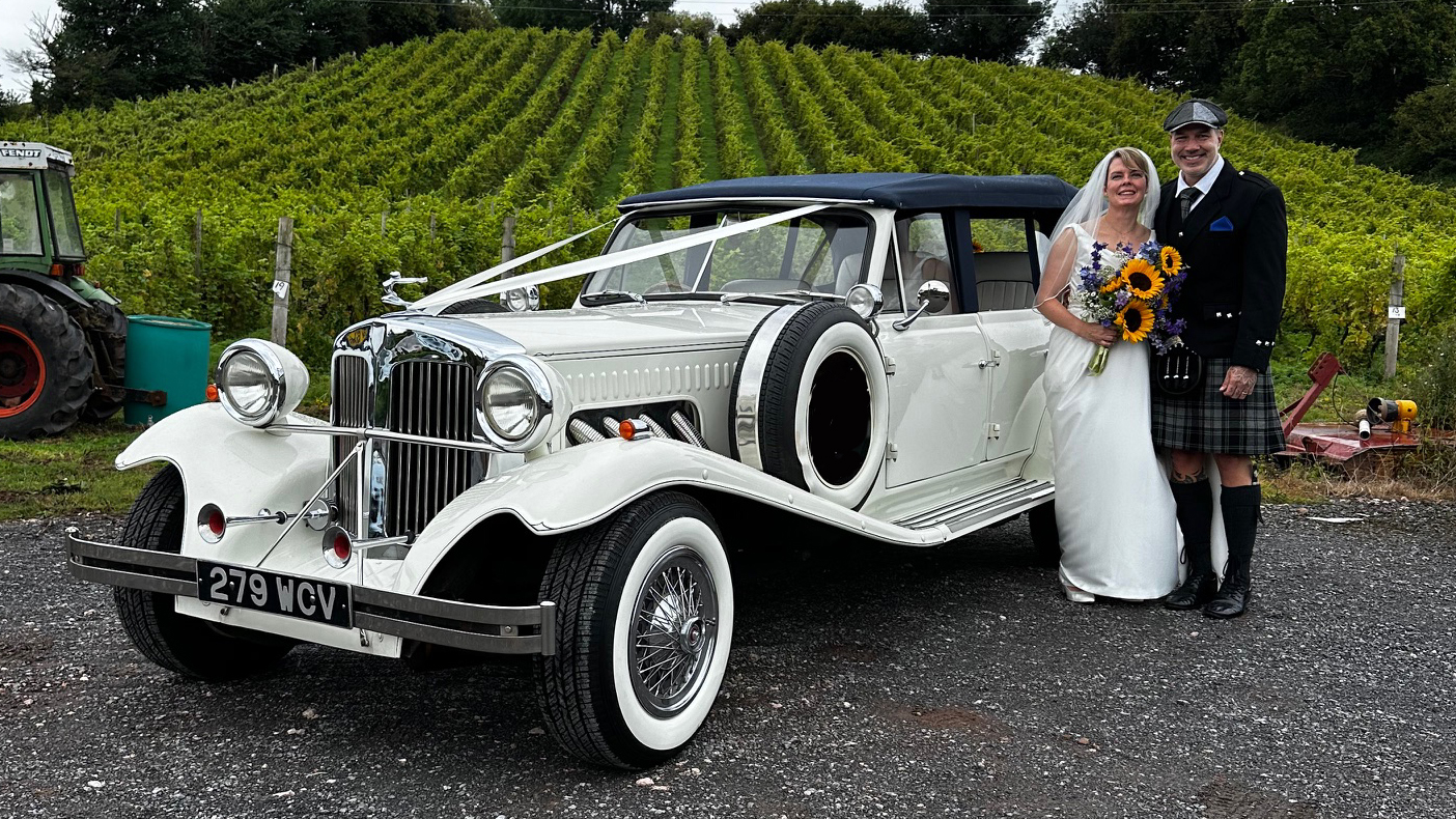 Bride and Groom standing next to a vintage Beauford decorated with white ribbons