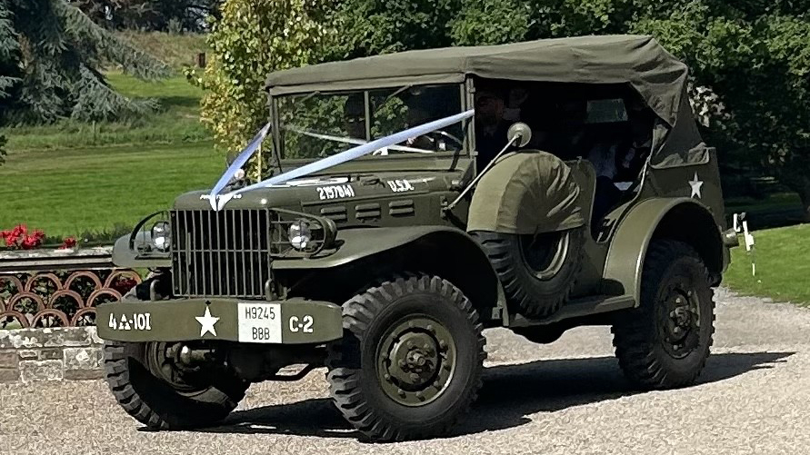 Military army Dodge car with a Khaki Green soft top canvas, decorated with pale blue Ribbons parked in frotn of a wedding venue