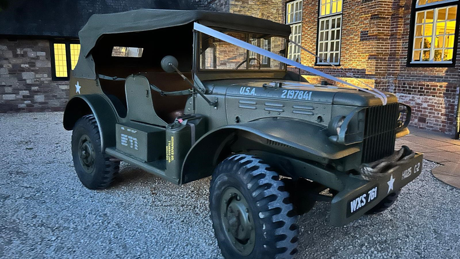 Army Military vehicle at dusk with wedding ribbons accross front bonnet parked in front of a wedding venue