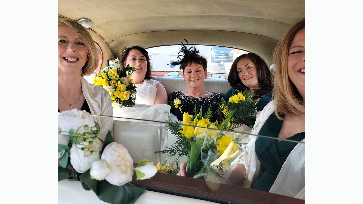 Bride and Bridal Party seating and smiling in the rear compartment of austin princess. Photo taken front the front seat through the glass divider. Bridal party holding yellow tulips.