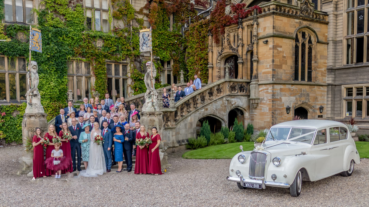 Classic Ivory Austin Princess Limousine parked in front of Carlton Towers wedding venue in Goole with wedding guests standing on the stairs outside the main entrance of the venue