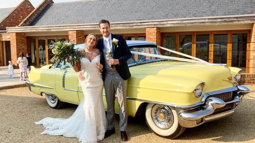 Bride and Groom standing in frotn of a classic yellow Cadillac in front of the wedding venue