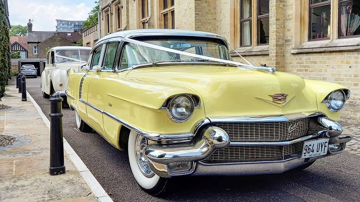 Classic Yellow cadillac decorated with white ribbons parked in front of a cathedral  followed by a second classic car