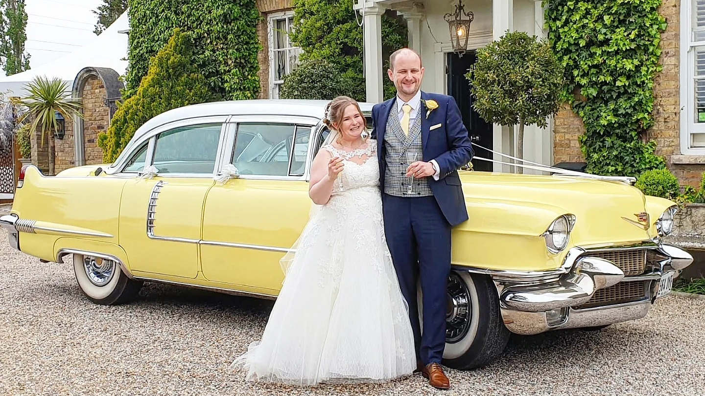 Bride and Groom holding each others in front of a Classic yelow american Cadillac