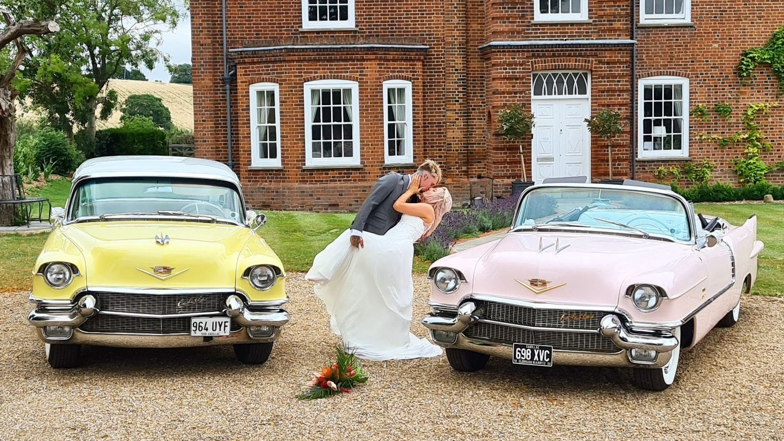 Bride and Groom kissing in the middle of two classic American Cadillac. The left car is Yellow and the second one on the right is Pink.