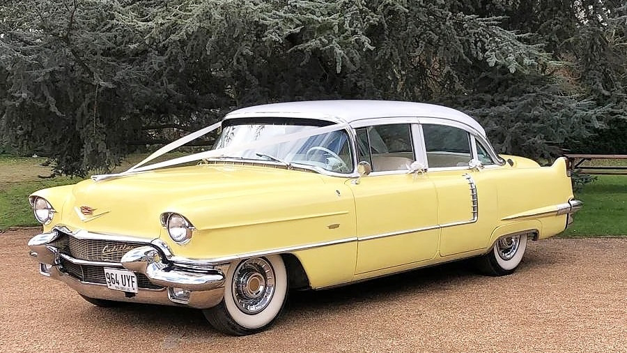 Front left view of classic american cadillac with white roof and dressed with traditional V-shape ribbons accross its bonnet.