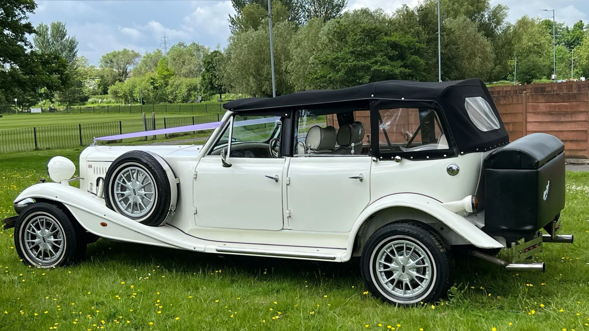 Left side view of vintage Beauford with Black soft top roof, black picnic trunk at the rear and spare wheel mounted on side of the vehicle