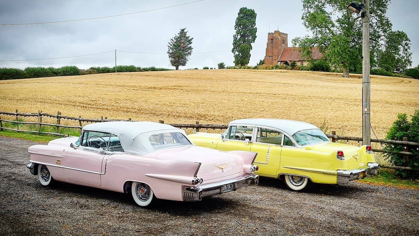 Fin tails rear view of two classic cadillacs in yellow and pale pink parked in the Countryside