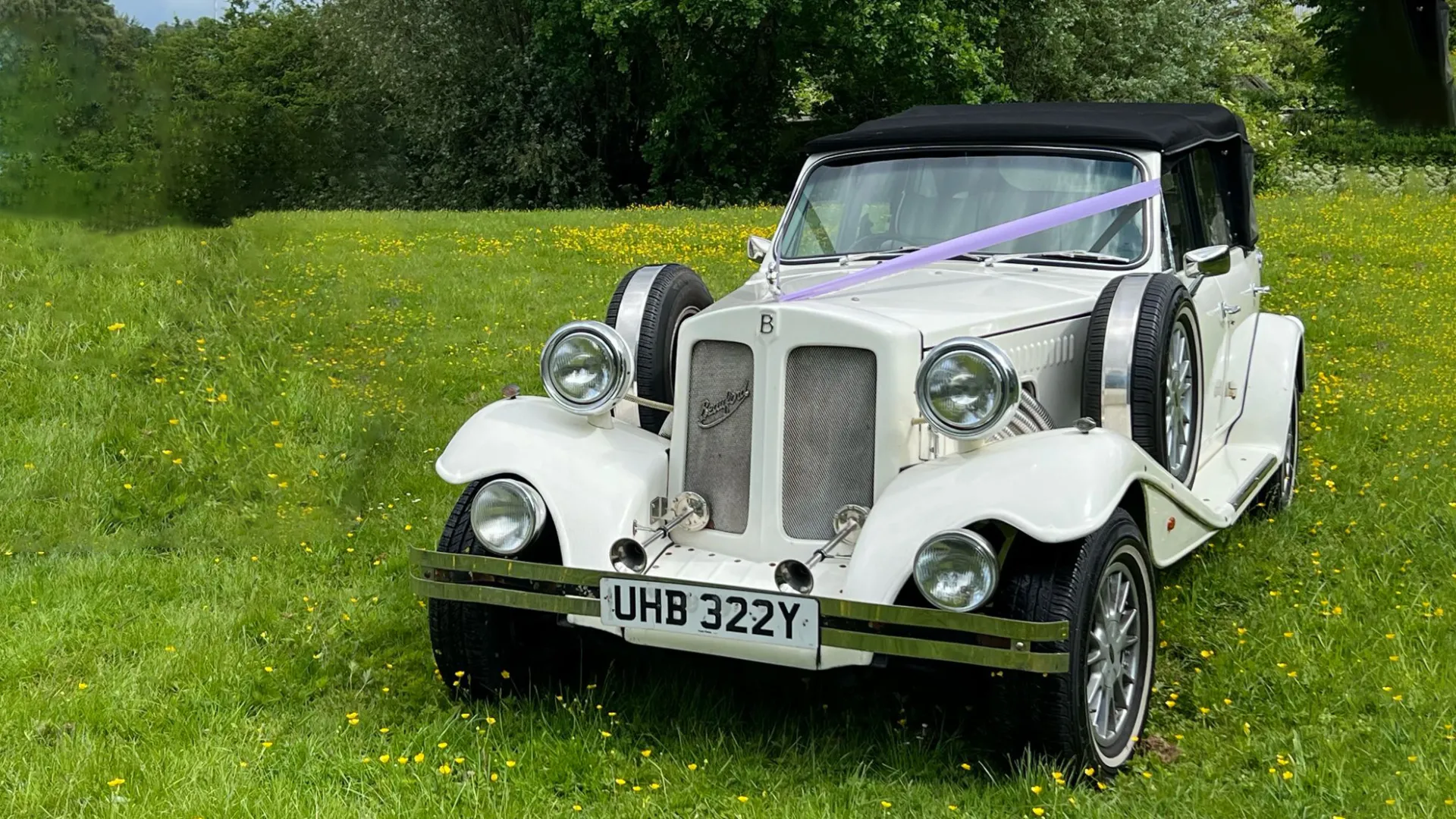 Vintage Beauford in Ivory with black soft top roof decorated with lillac wedding ribbons in a green field