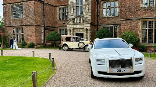 Modern Rolls-Royce Ghost in White parked in front of a small wedding venue in Coventry. Bride and Groom can be seen in the very far background walking holding hands.