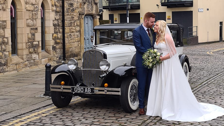 Bride and Groom holding each others n front of black and Ivory Bramwith limousine