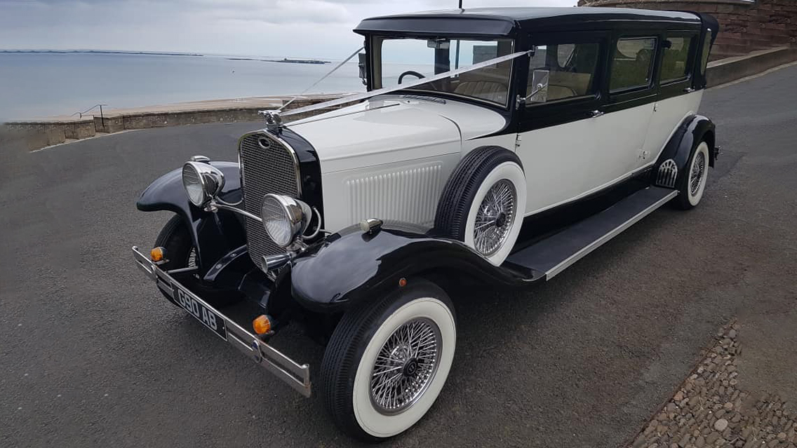 Black and Ivory Bramwith Limousine decorated with white ribbons parked on the road with sea in the background