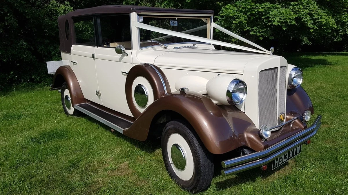 Convertible Vintage Regent in Bronze and Ivory decorated with White ribbons in a green field. Brown Soft Top roof is closed