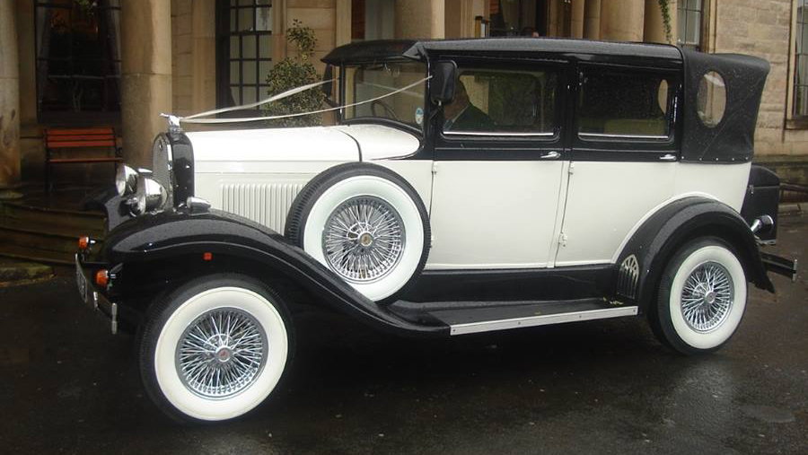 Left side view Badsworth Landaulette with black soft top roof closed, large white wall tires, spokes wheels and spare wheel mounted on the side of the vehicle