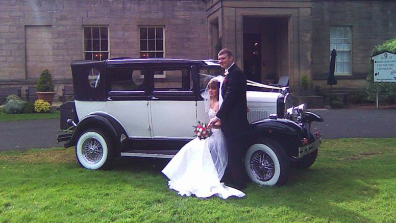 Badsworth Landaulette in Ivory with Black skirts and black roof. Bride and Groom are standing by the vehicle posing for photos