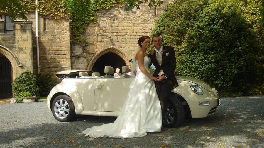 Bride and Groom holding each others in fronmt of a cream modern Volkswagen Beetle wedding car