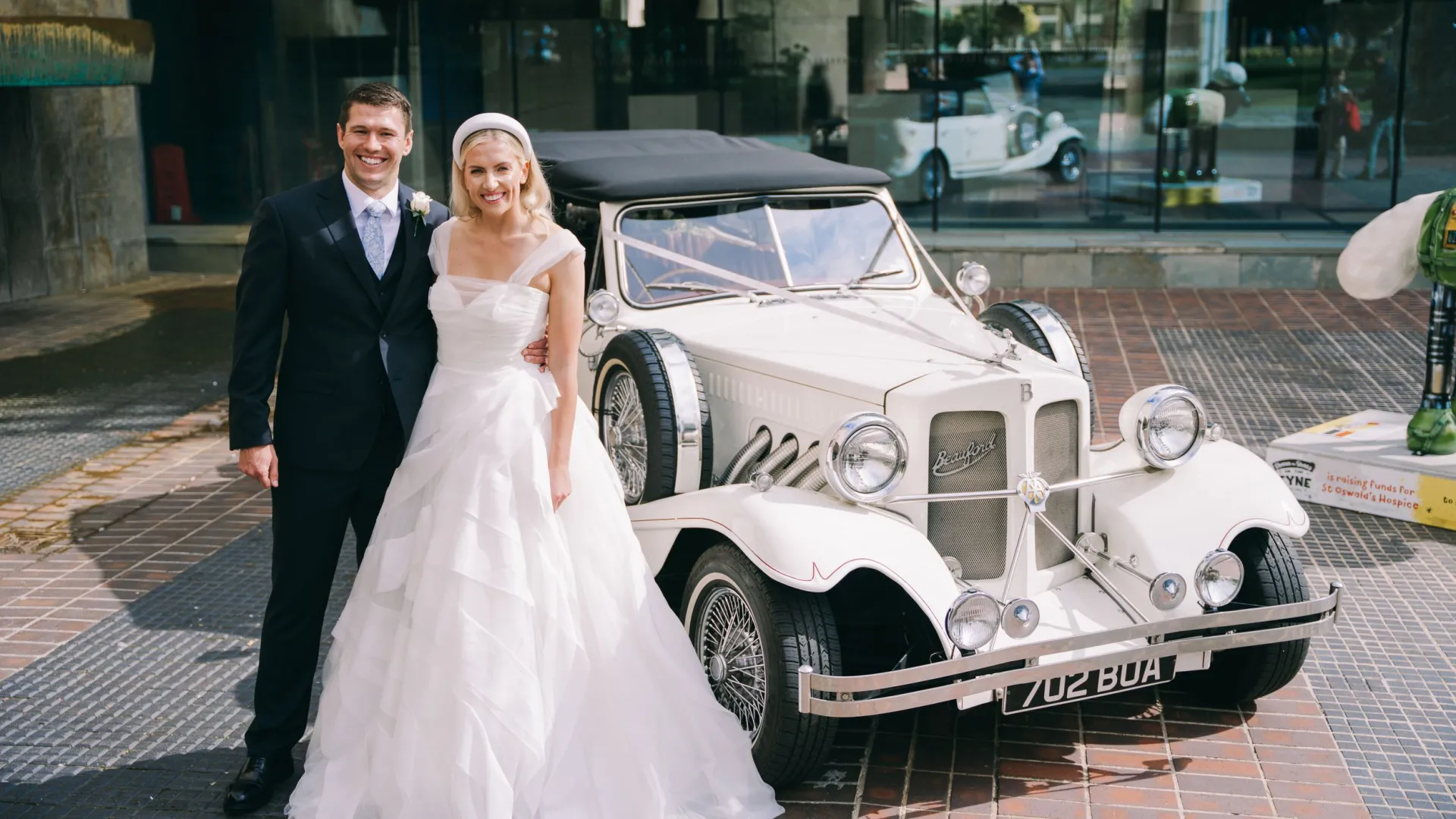 Bride and Groom standing in front of Ivory Beauford Convertible with Black roof