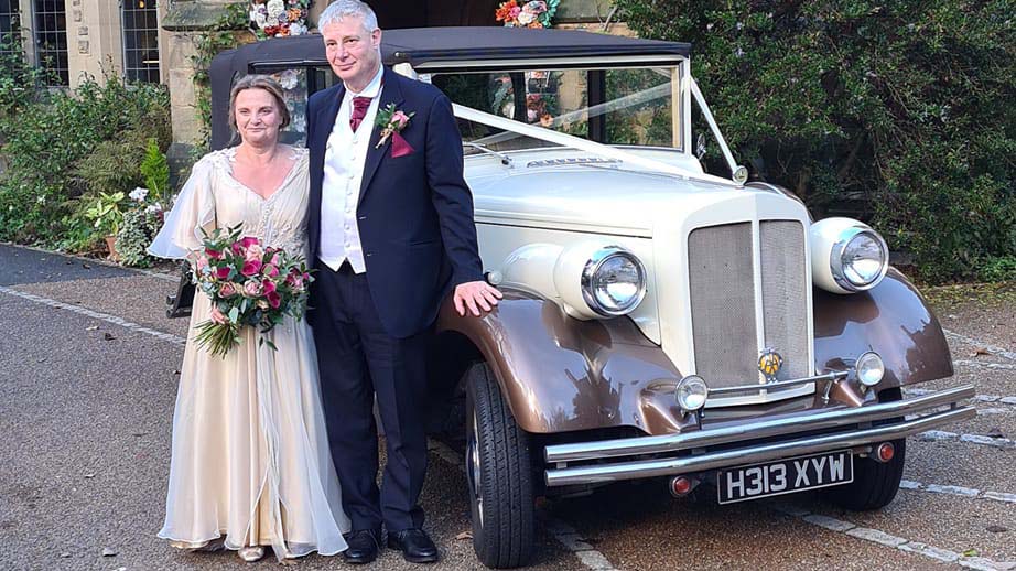 Bride and Groom standing in front of Vintage Regent with Bronze wheel arches and Ivory on the side and Bonnet