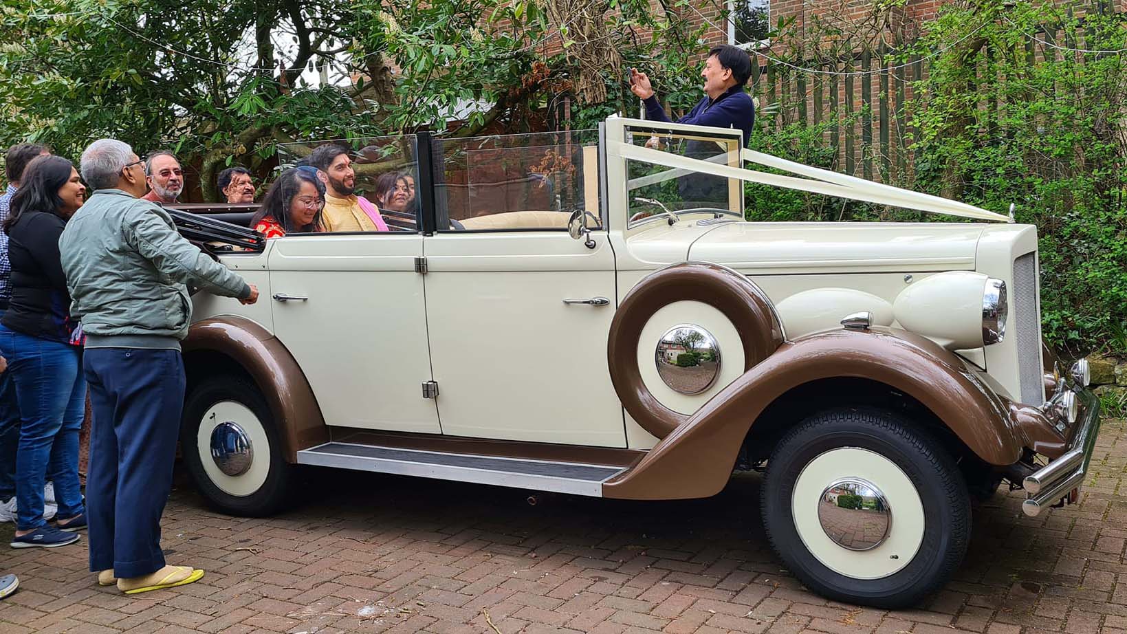 Asian Couple seating inside the vintage regent wedding car with roof down and wedding guests all around the car.