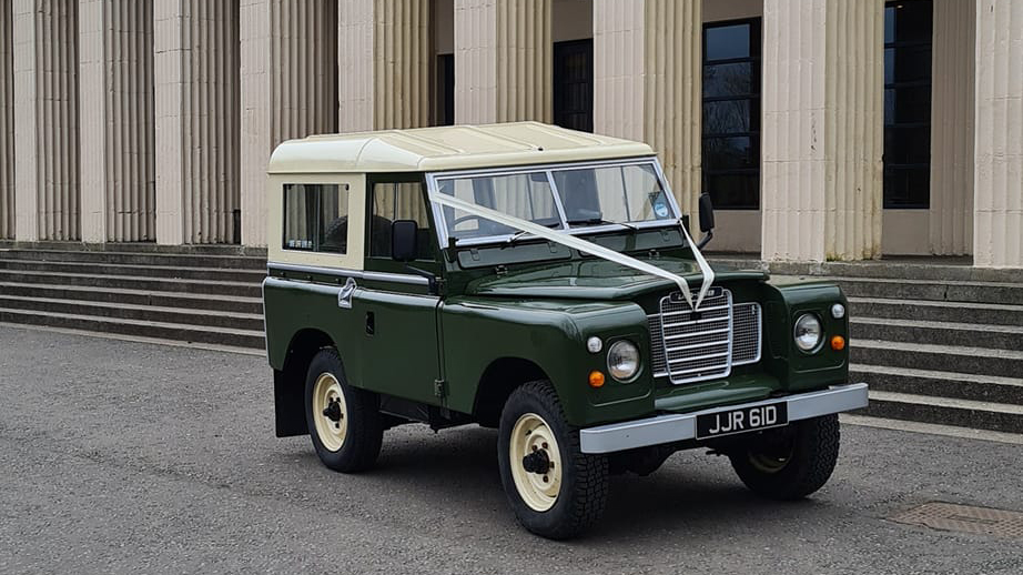 Green and White Classic Landrover decorated with White ribbons in front of wedding venue