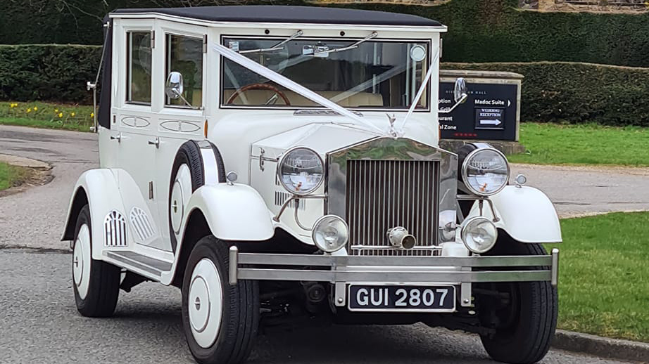 Front view of a White Imperial Convertible dressed with wedding ribbons accross its bonnet.