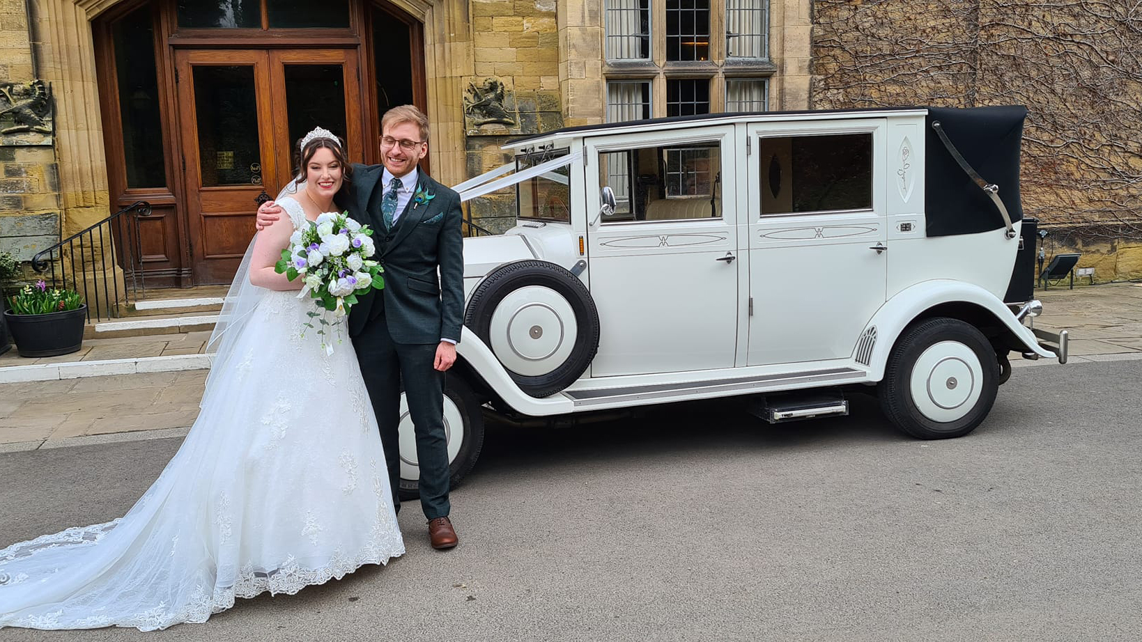 White Imperial Convertible with black soft top roof closed. Bride holding a bouquest of flowers with her groom standing next to her.