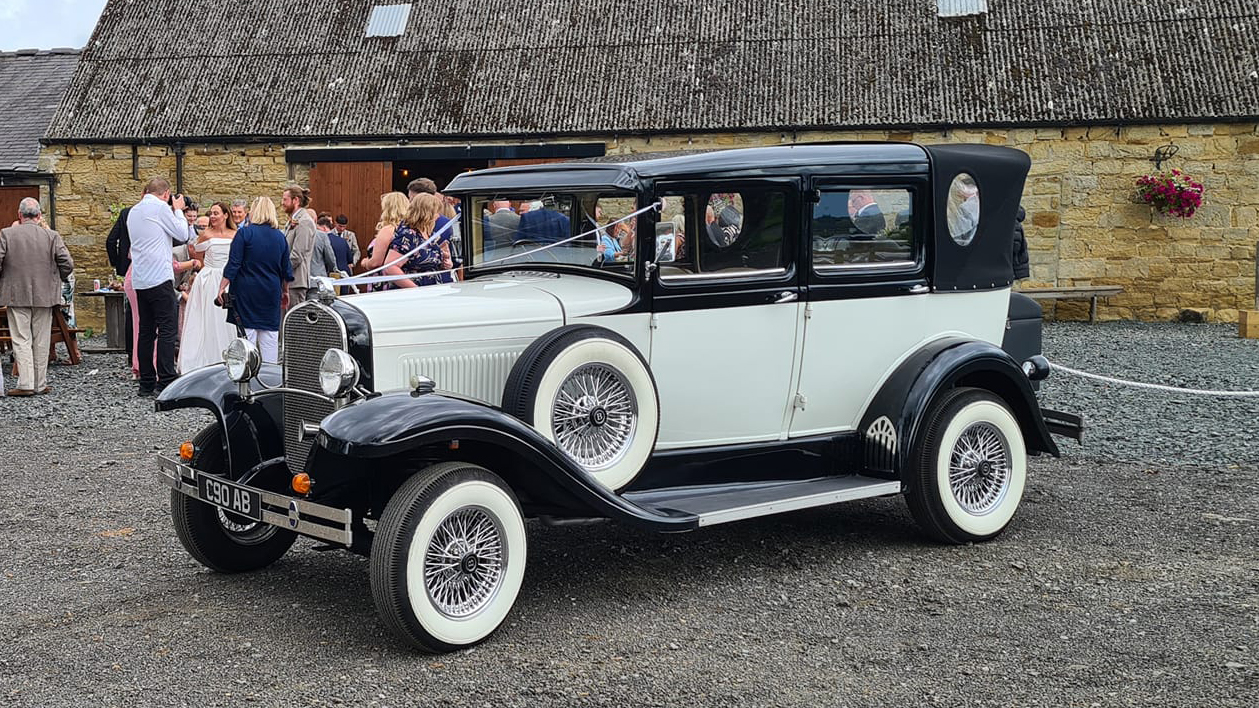 Badsworth Landaulette in Black and ivory dressed with ribbons in front of wedding venue in Newcastle. Wedding Guests can be seen in the background