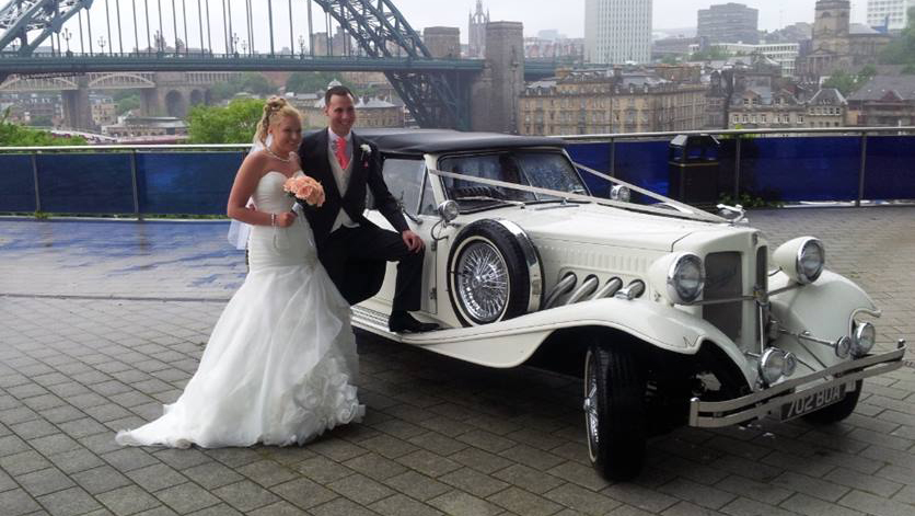 Beauford Convertible with Bride and Groom standing by the vehicle posing for photos.