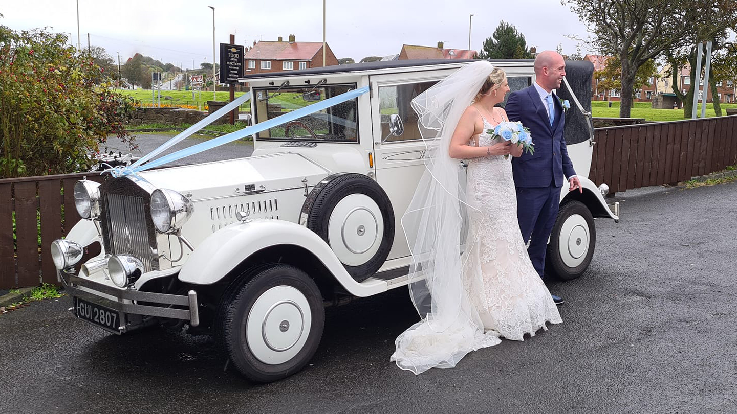 White Imperial Convertible decorated with light blue ribbons with Bride and Groom standing by the vehicle