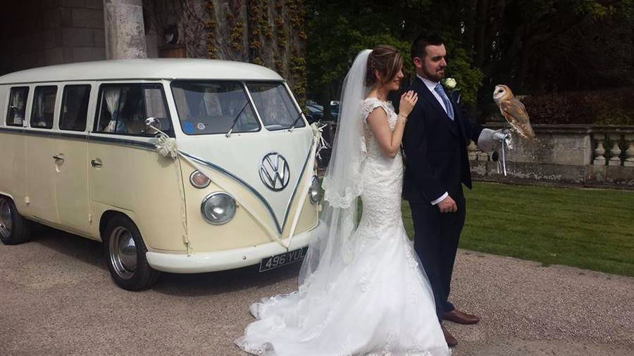 Bride wearing a White wedding dress and Groom a a dark blue suit holding a bird in his left hand are standing in front of a Classic VW Campervan