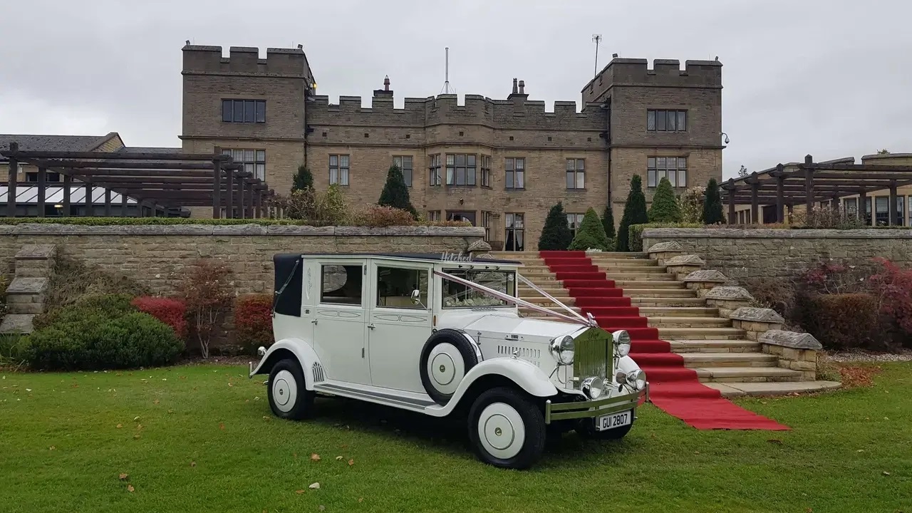 White Imperial Convertible parked at wedding venue. Long red carpet layed down from the car to the entrance of the venue