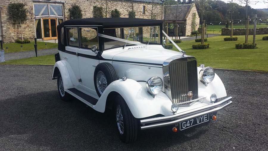 White Regent Convertible with black roof dressed with White Ribbons accross its front bonnet parked at a wedding venue