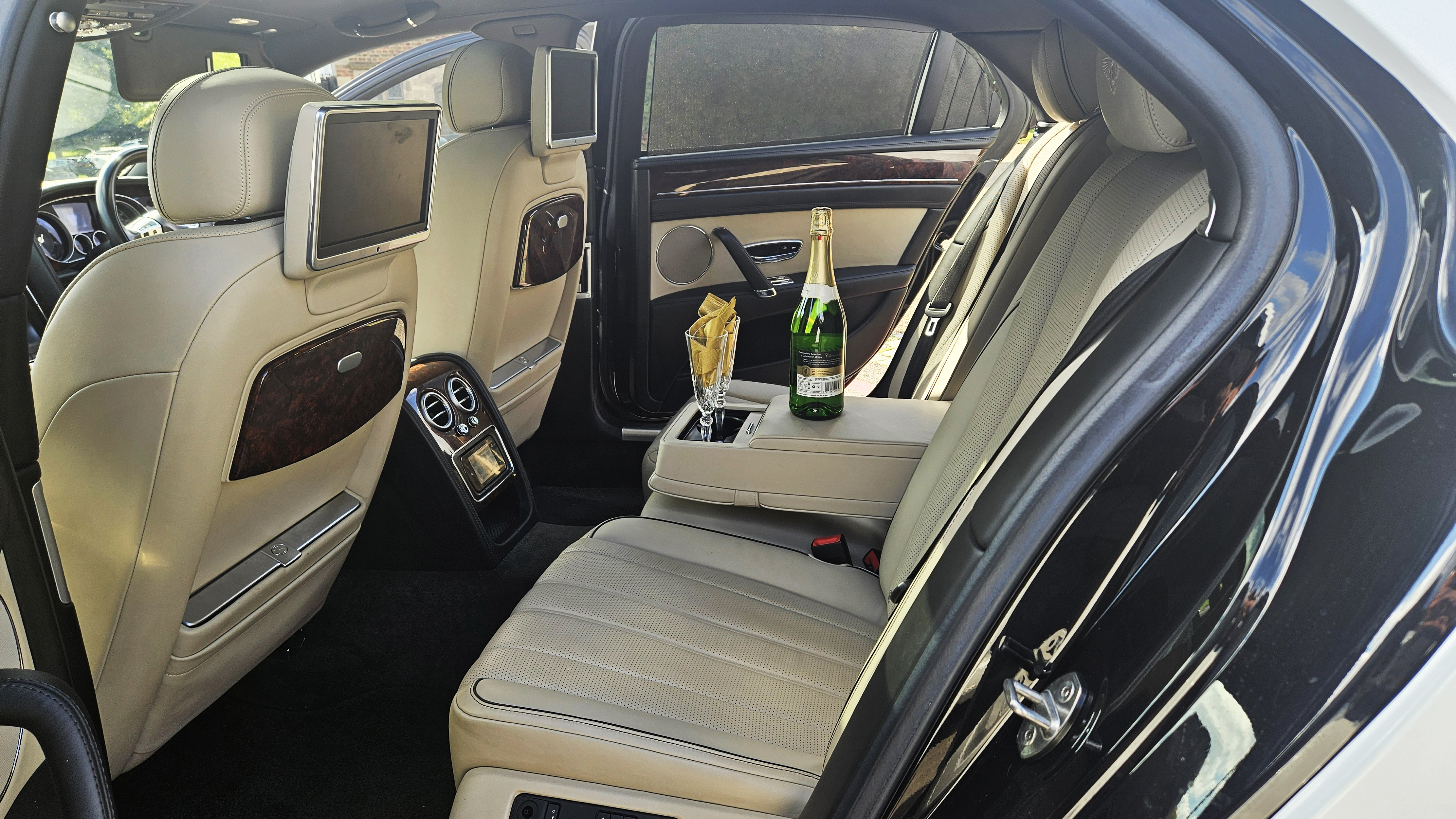 Rear interior inside Bentley with cream quilted leather, wooden picnic table and entertainment system