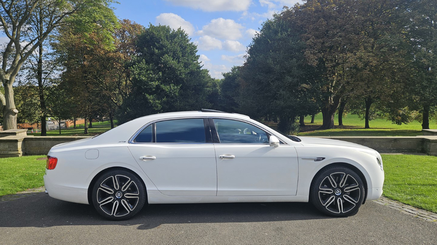 Right side of White Bentley parked accross a path in a park