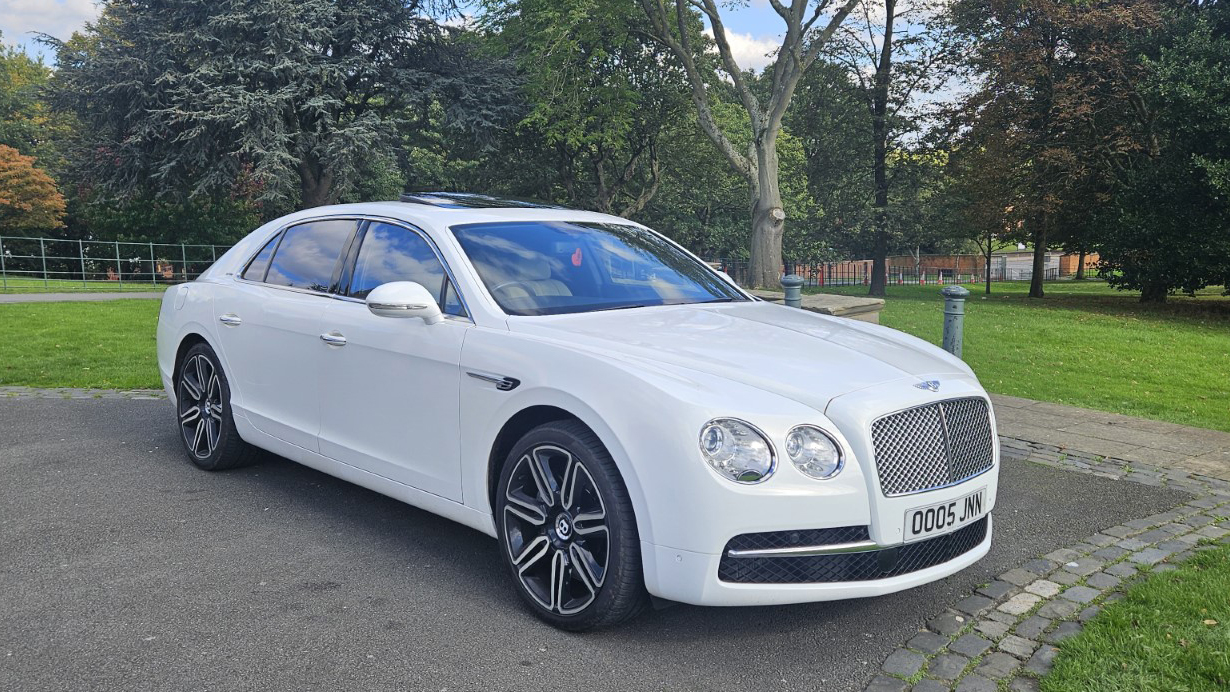 Front right side View of White Bentley Flying Spur with Mulliner specs, large black and silver alloy wheels, chrome front grill