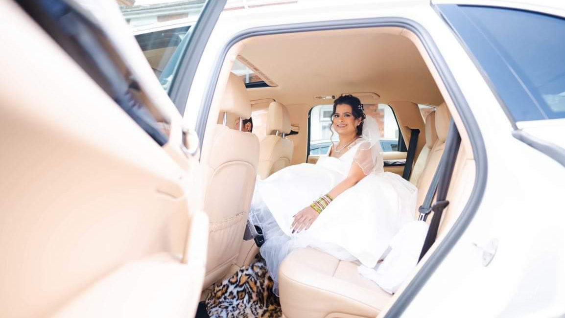 Smiling Bride wearing a white dress seating inside a White porsche cayenne with cream leather seats.