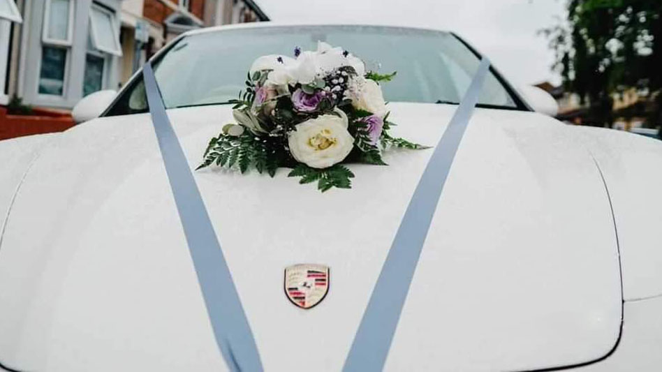 Blue ribbons on the bonnet of a white modern car with posy of lfowers in the middle