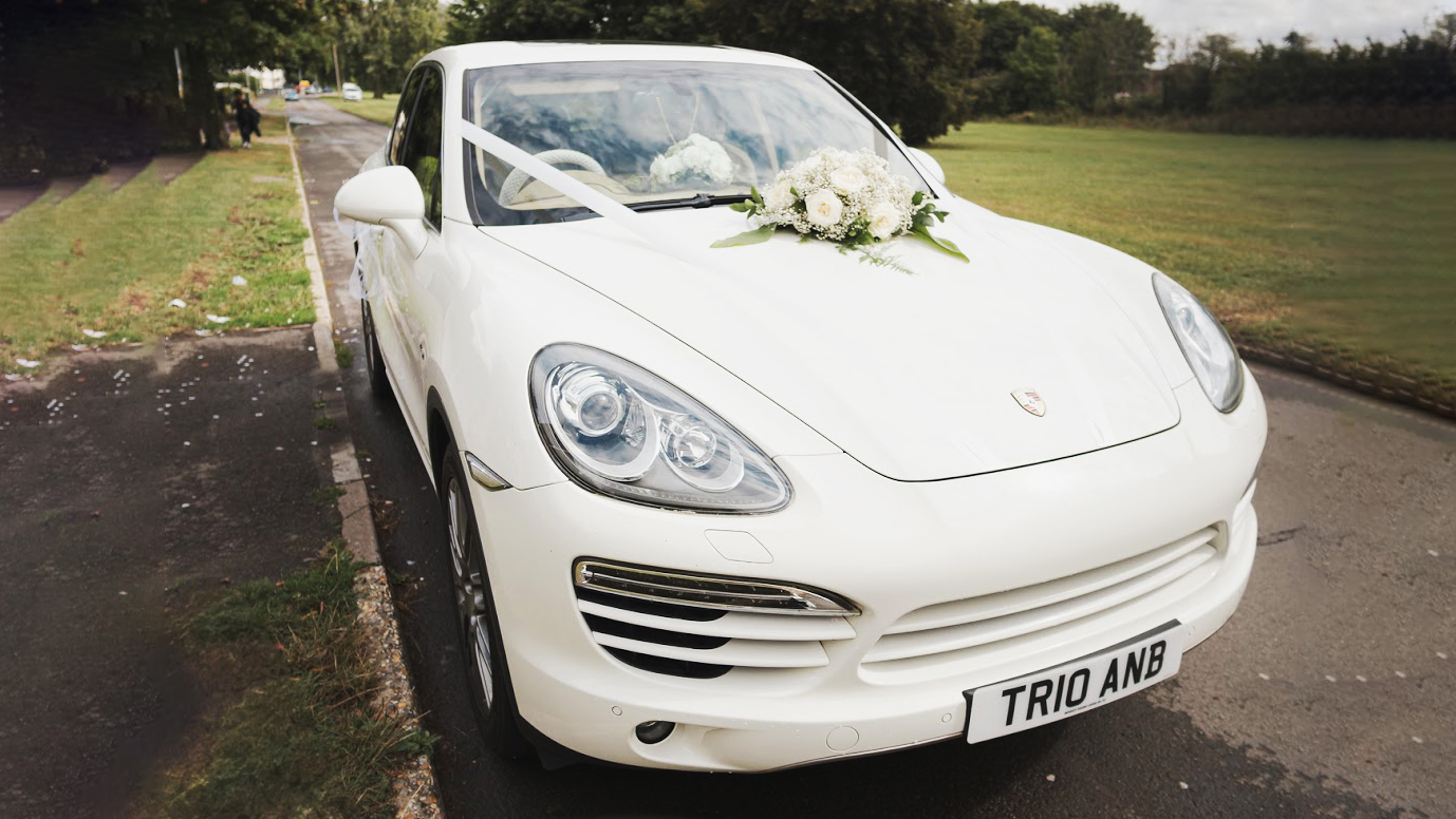 White Porsche Cayenne decorated with white ribbons and flower decorated on its front bonnet.