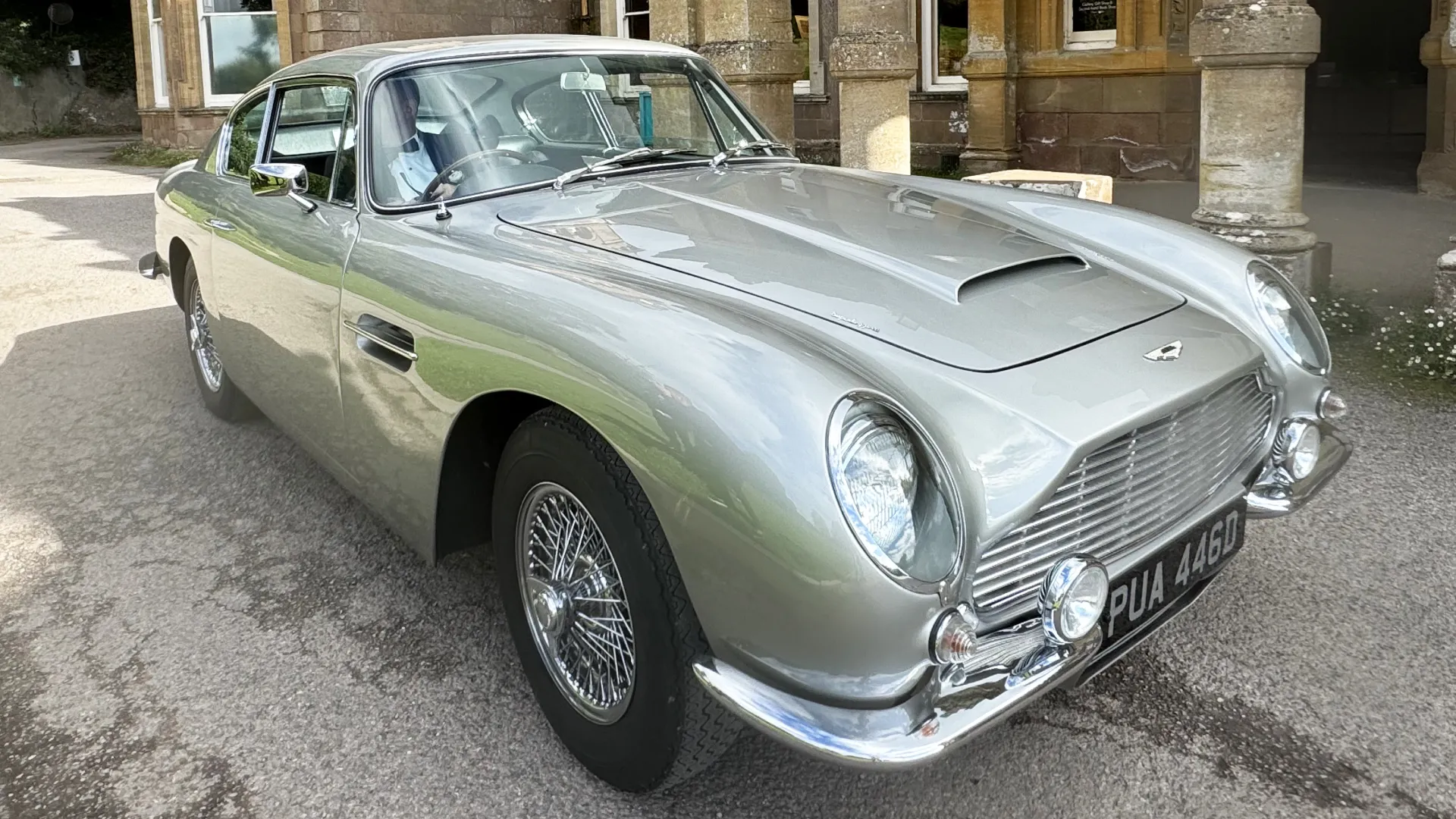 Silver Aston Martin DB6 parked in front of wedding venue.