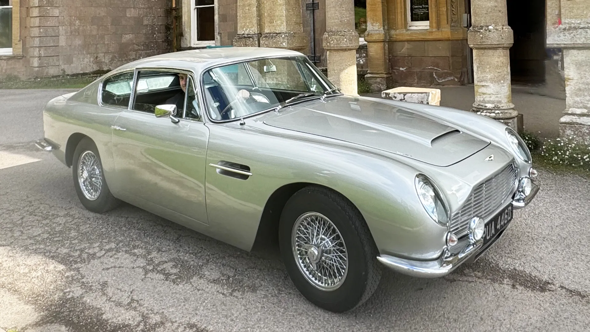 Silver Aston Martin DB6 parked in front of wedding venue.  Chrome spoke wheels.