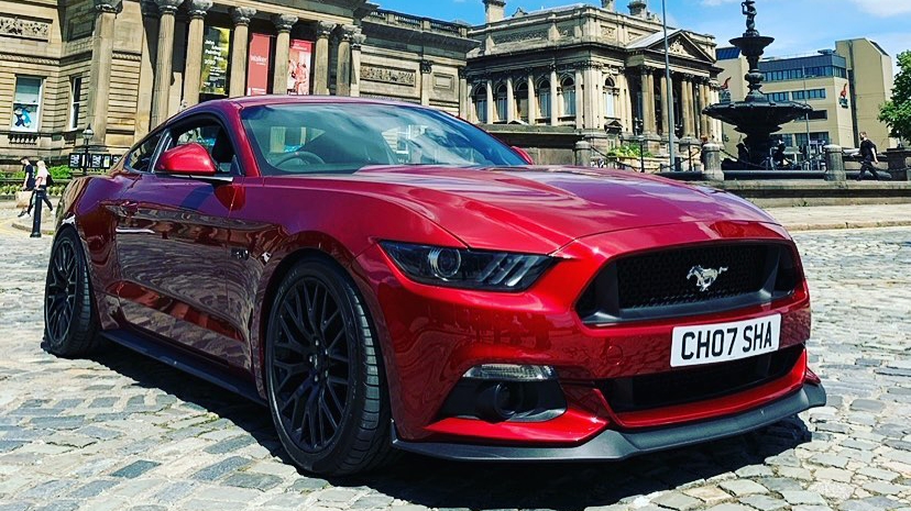 Cherry-red Modern Ford Mustang GT Fastback with black alloy wheels parked in front of wedding venue in Stafford