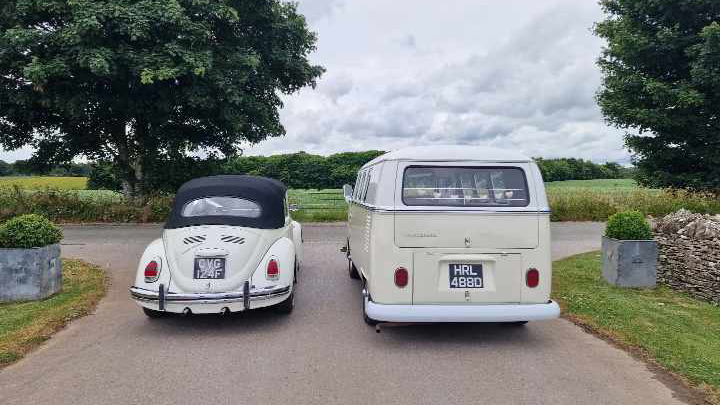 Rear view of retro VW Campervan and Beetle parked next to each others. Beetle has its black soft top roof closed up.