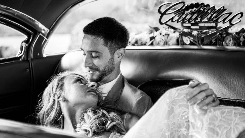 Black and White photo of Bride and Groom seating in the rear of a Cadillac bench seat.