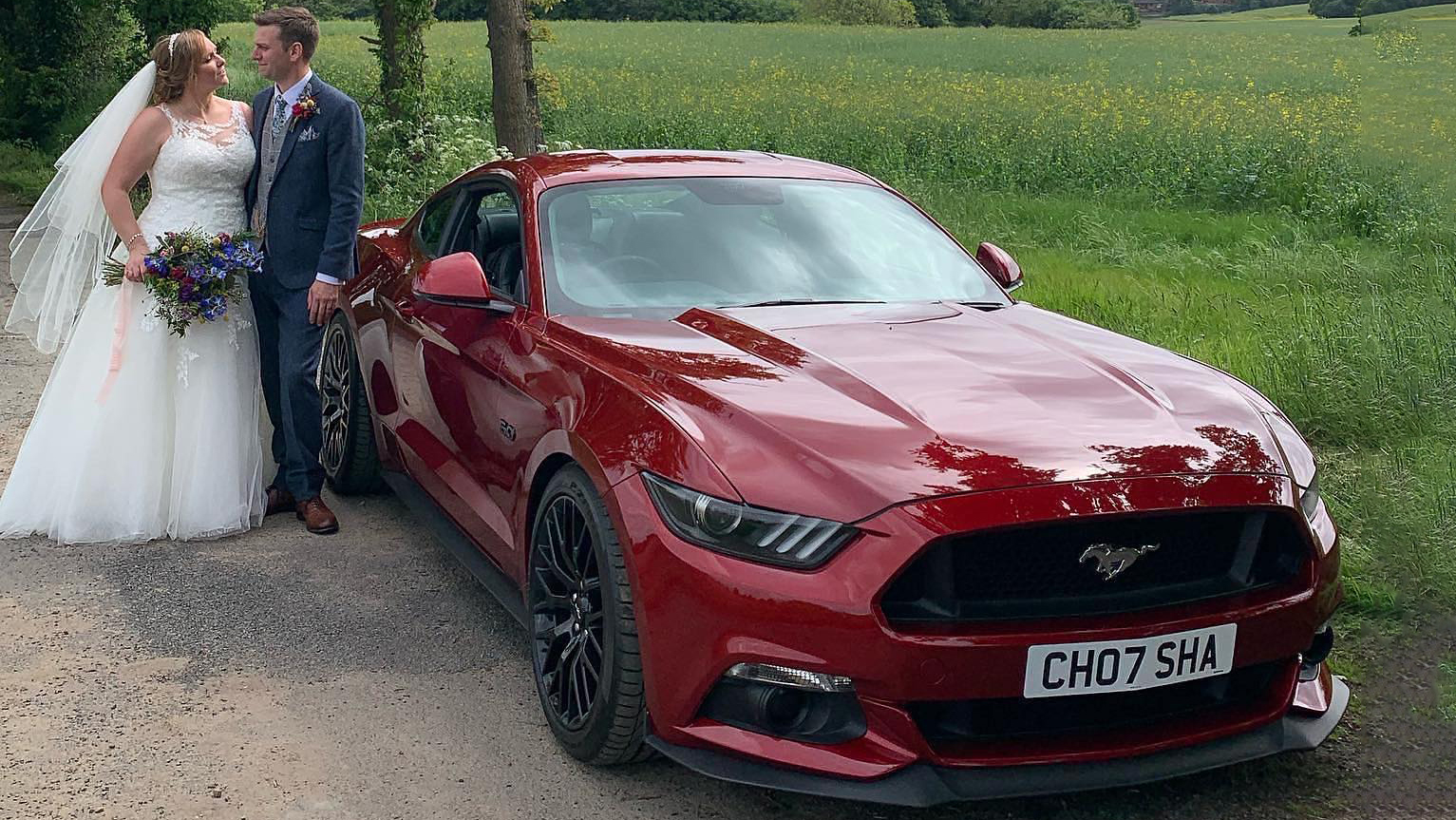 Bride and Groom standing next to a modern Ford Mustang in Cherry red