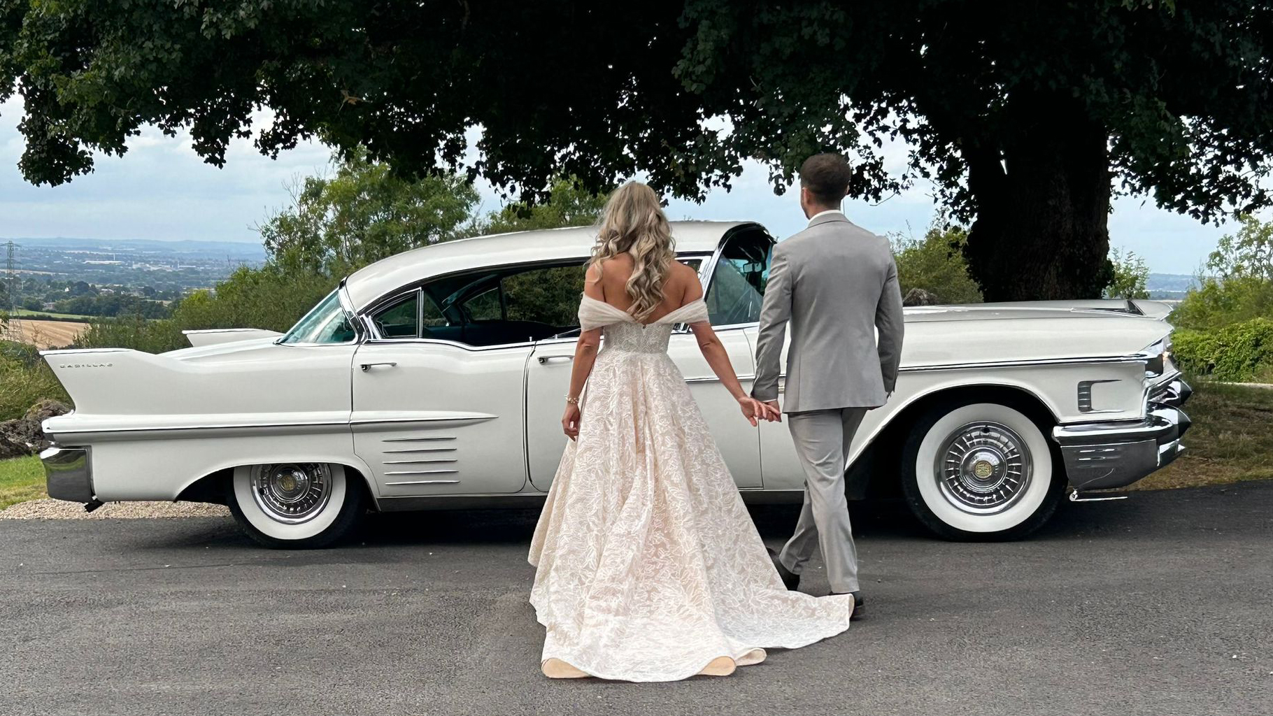 Bride and Groom holding hands walking towards a white american cadillac